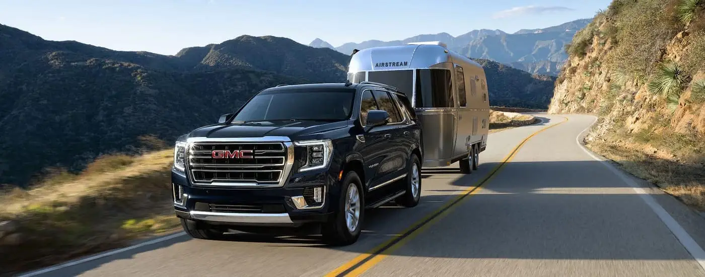 A black 2022 GMC Yukon is shown towing an airstream camper on a mountain road.