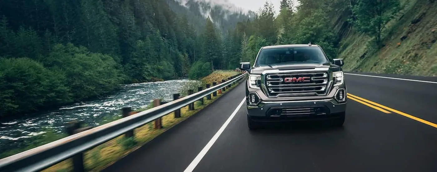 A grey 2020 GMC Sierra 1500 is shown from the front driving on a road next to a river.
