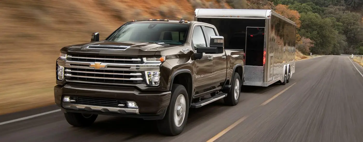 A black 2021 Chevy Silverado 2500 HD is shown towing a trailer on a highway.