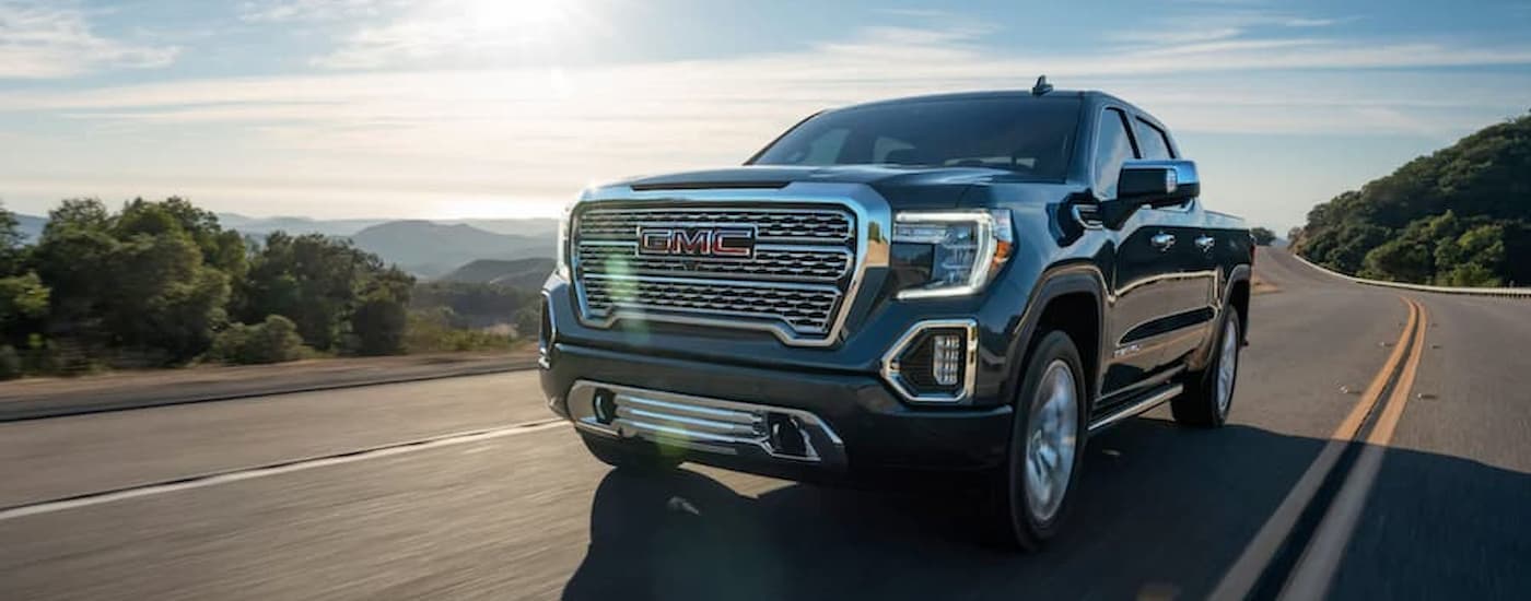 A black 2020 GMC Sierra 1500 Denali is driving on an open road with a mountain view.