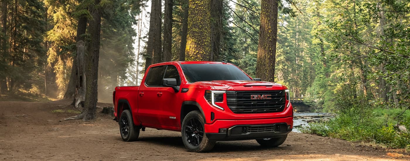Red 2025 GMC Sierra 1500 parked off-road in a forest.