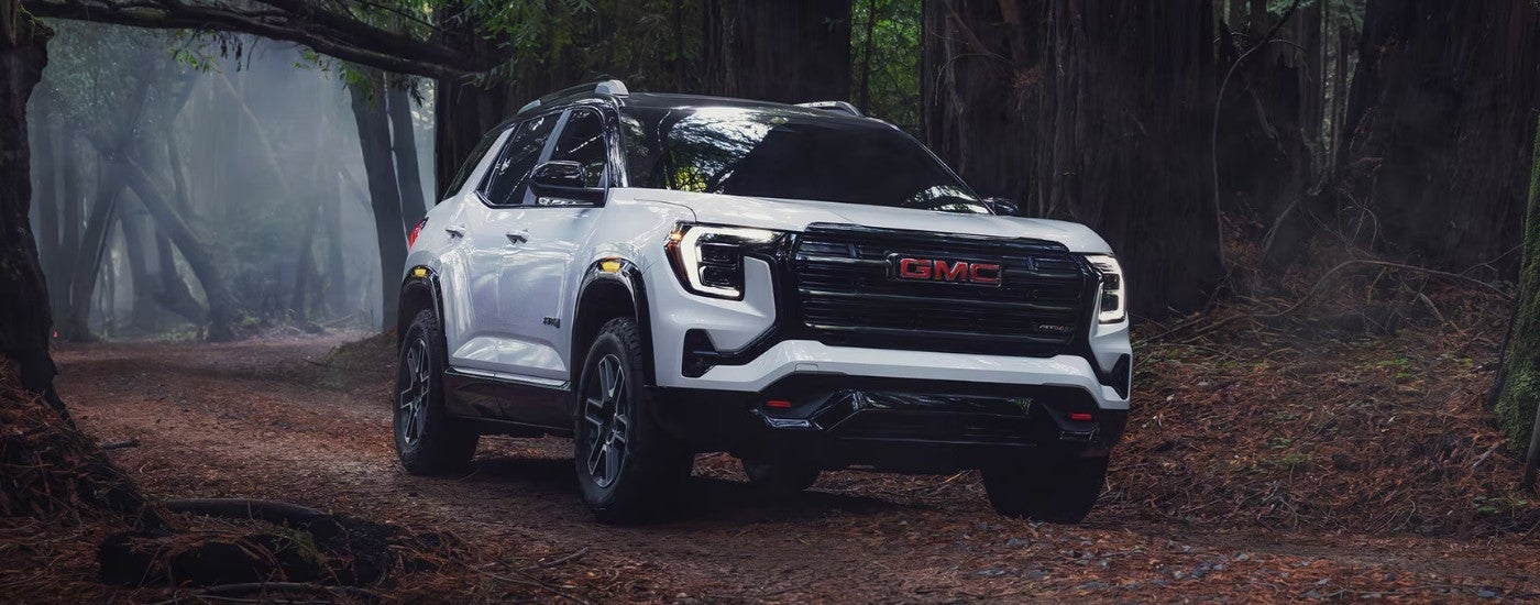 White 2026 GMC Terrain AT4 driving off-road through a forest.