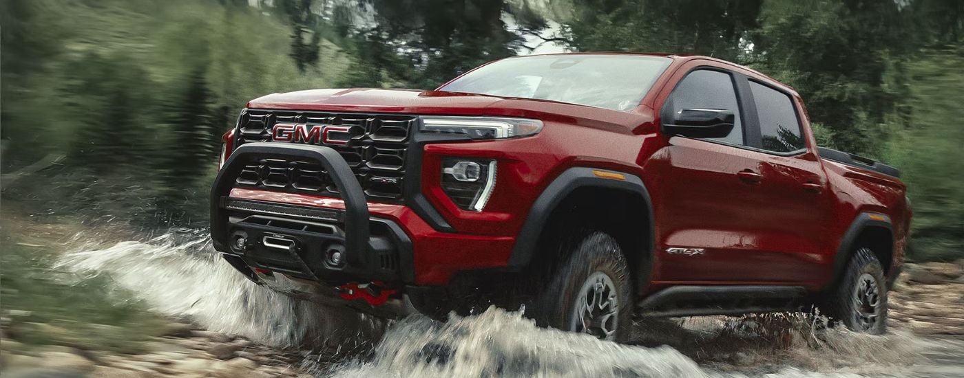 Red 2026 GMC Canyon AT4X driving through a river.