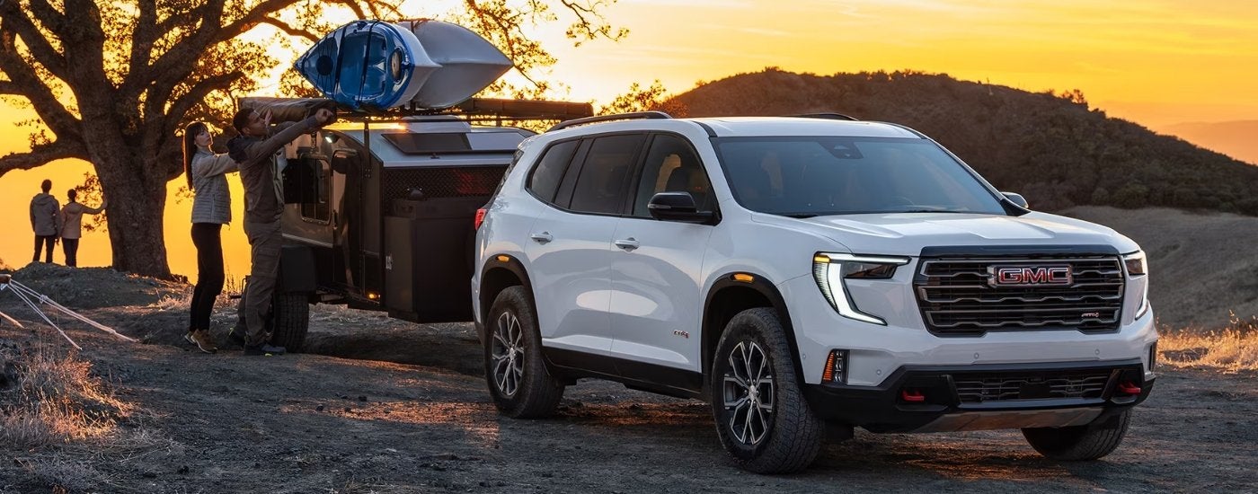 A white 2026 GMC Acadia AT4 towing a trailer at sunrise.