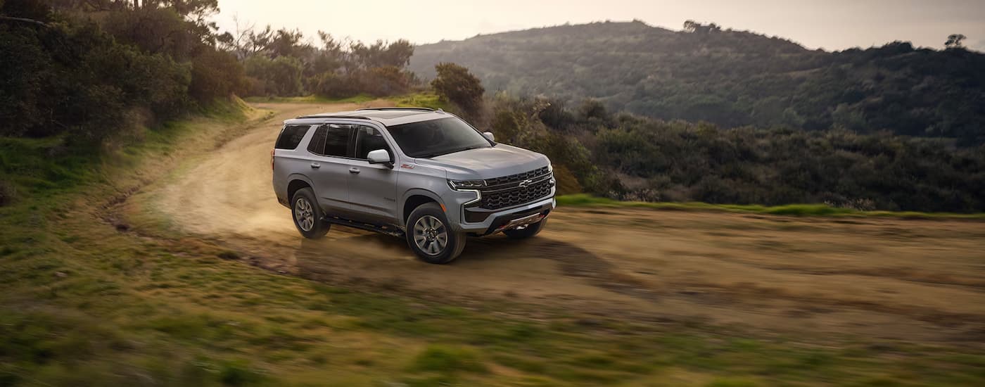 A silver 2024 Chevy Tahoe Z71 is shown driving on a dirt road.