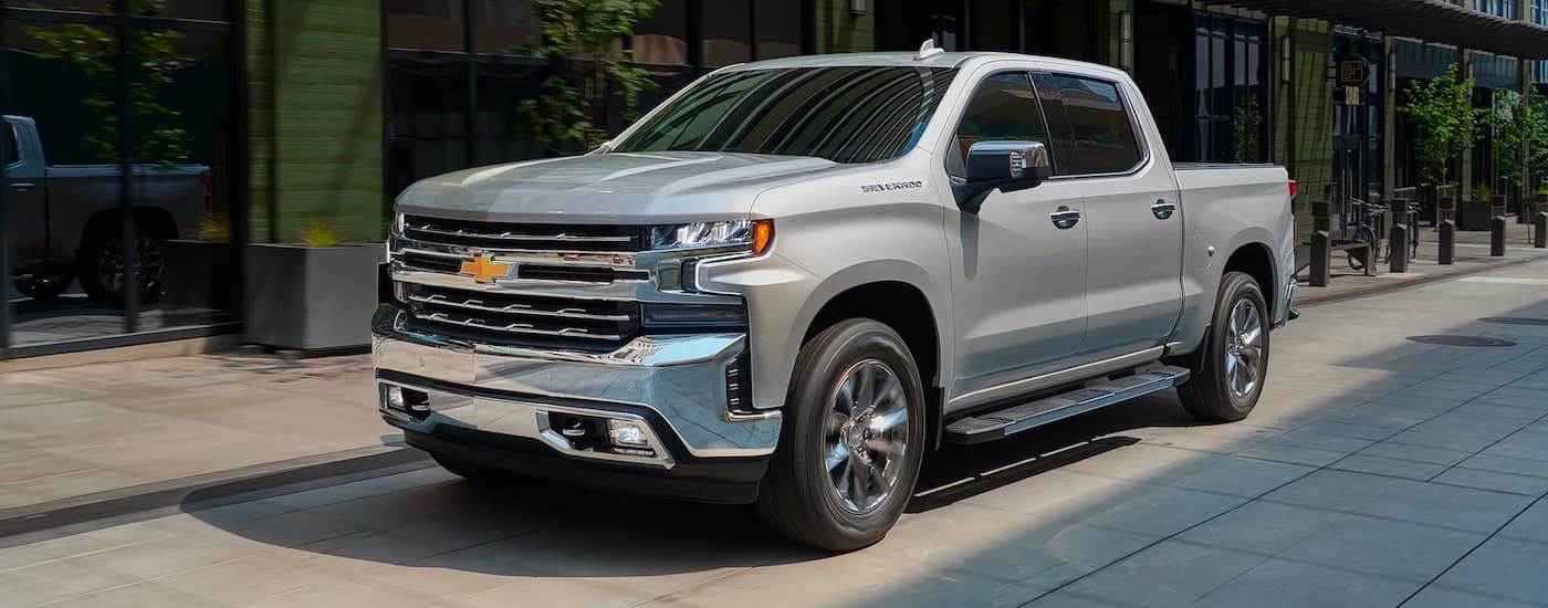 A silver 2021 Chevy Silverado 1500 is shown from the side parked on a city street.