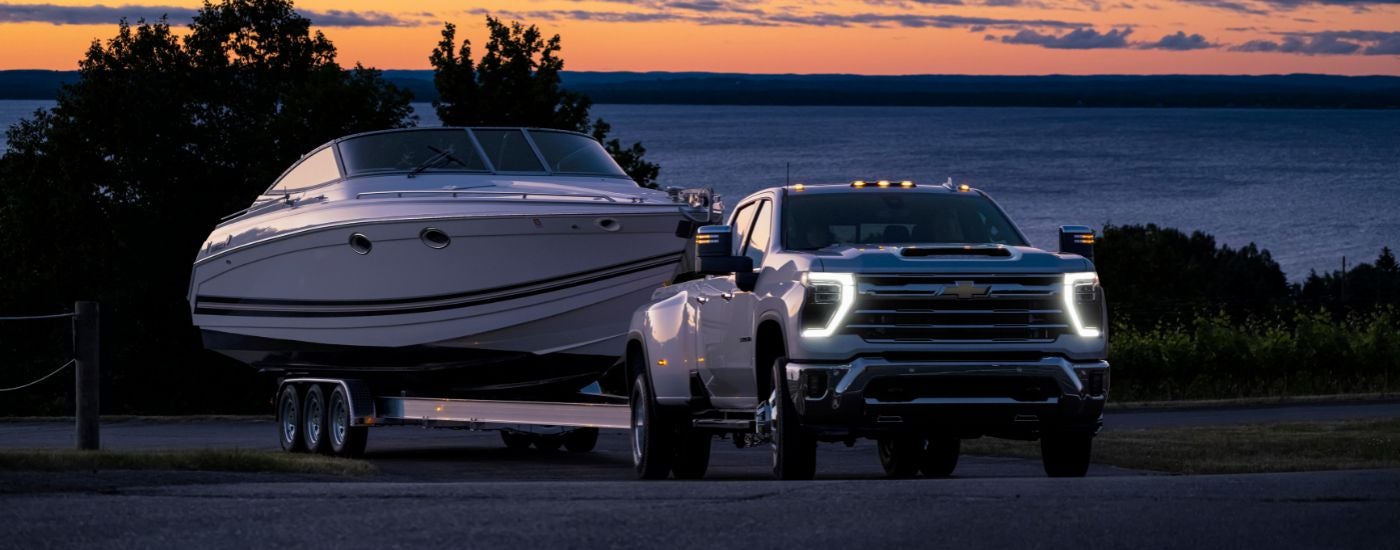 A white 2024 Chevy Silverado 3500 HD is shown towing a white boat on a trailer.