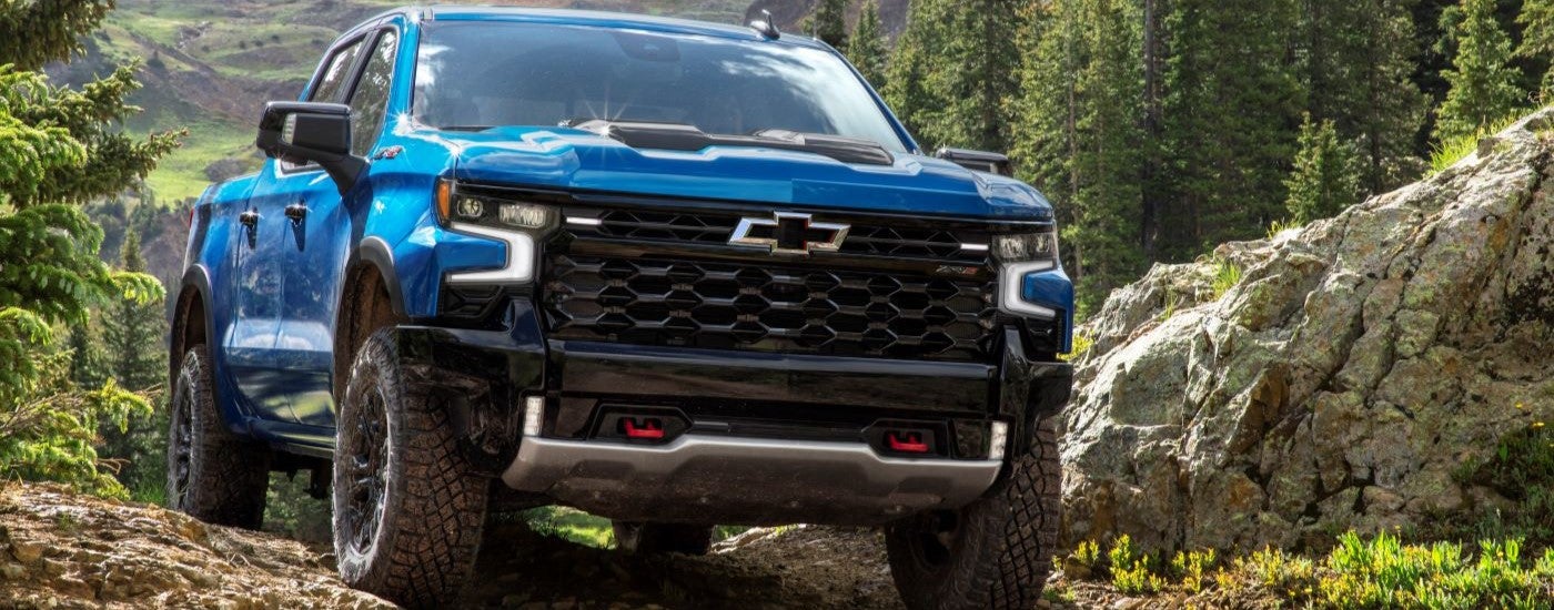 A blue 2024 Chevy Silverado 1500 ZR2 driving up a dirt hill.
