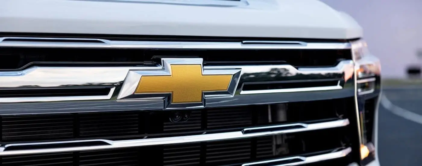 A close-up on the badge and grille of a white 2024 Chevy Silverado 3500 HD LTZ.