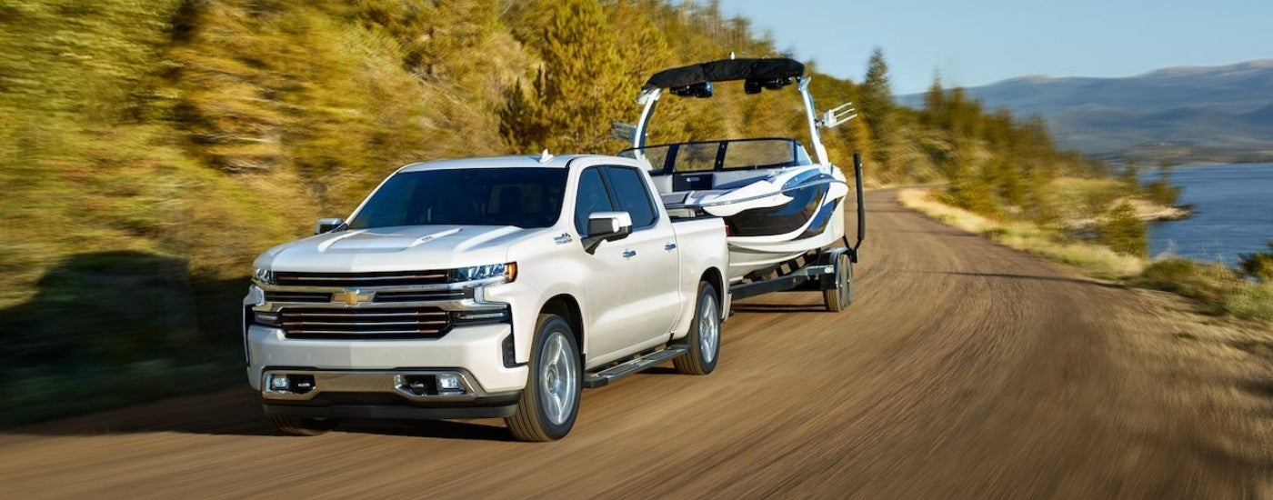 A popular Chevy Silverado for sale near New Albany, MS, a white 2021 Chevy Silverado 1500 High Country, is shown towing a boat.