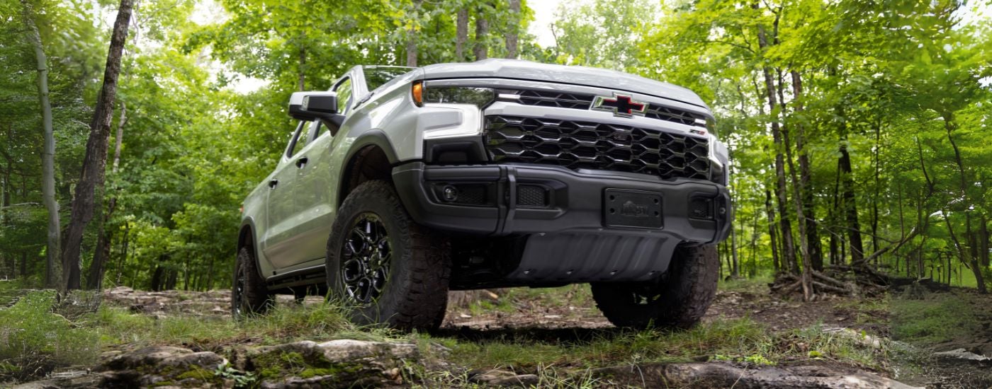 Low angle view of a white 2024 Chevy Silverado 1500 ZR2 parked off-road in a forest.