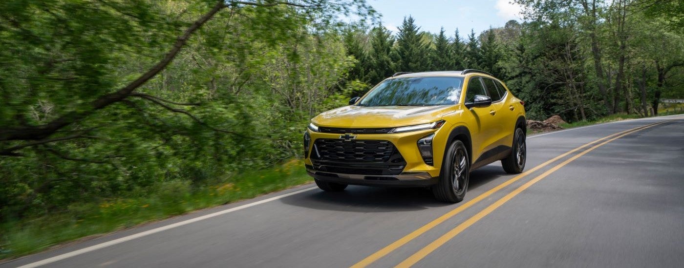 A yellow 2024 Chevy Trax ACTIV driving on a tree-lined road.