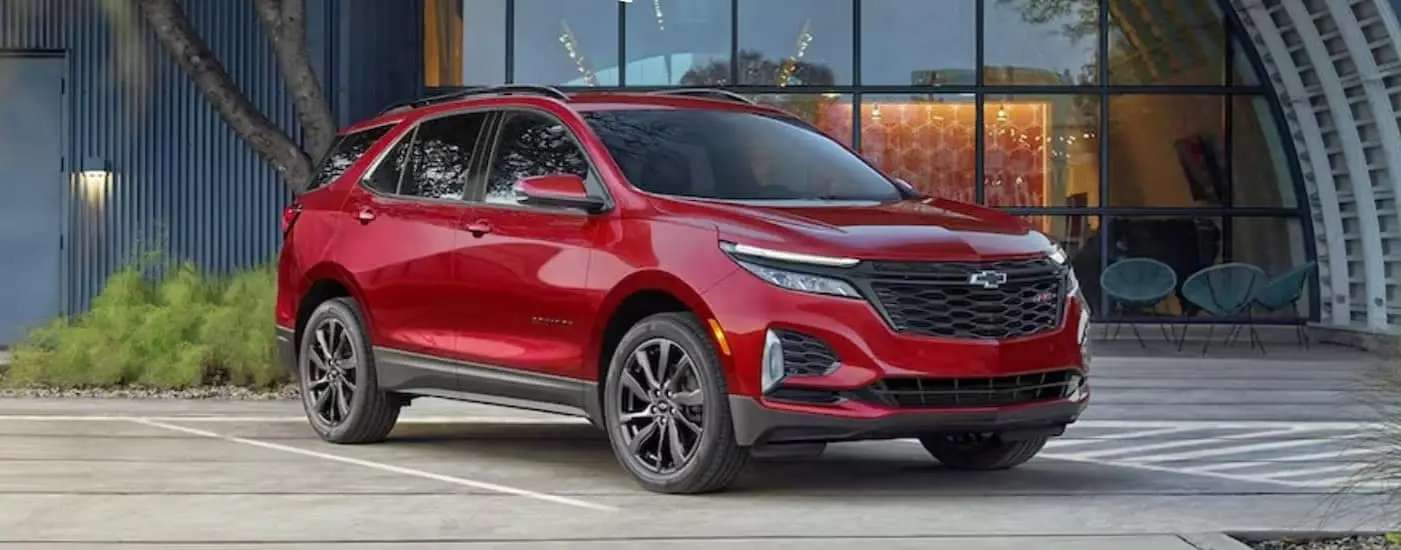 A red 2024 Chevy Equinox RS is shown parked near a hangar.