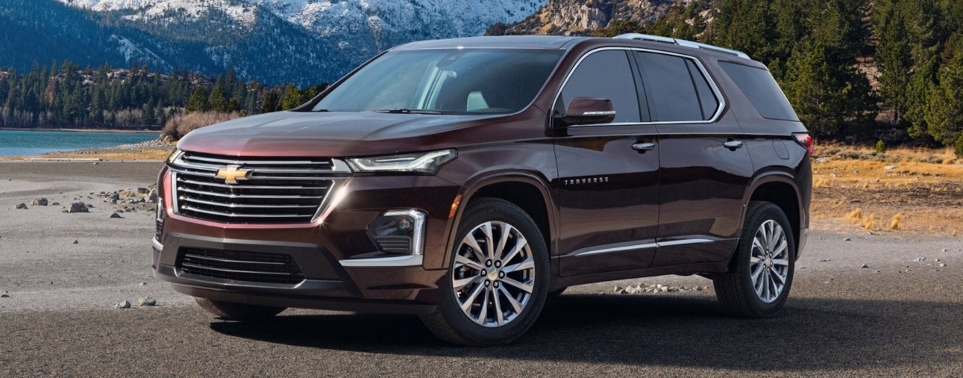 A purple 2022 Chevy Traverse High Country parked in front of a lake and mountains.