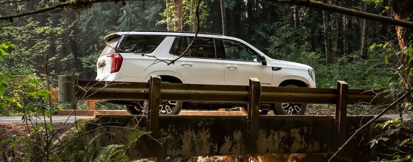 A white 2023 GMC Yukon AT4 is shown driving over a bridge.