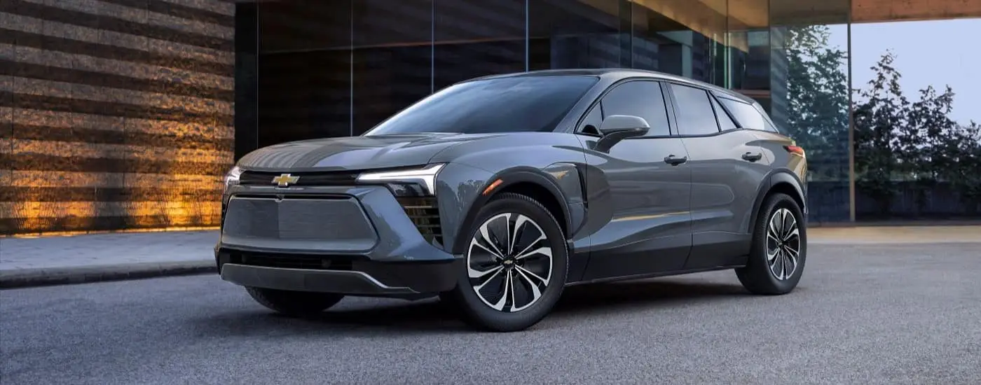 A grey 2024 Chevy Blazer EV is shown angled left while parked by a building.