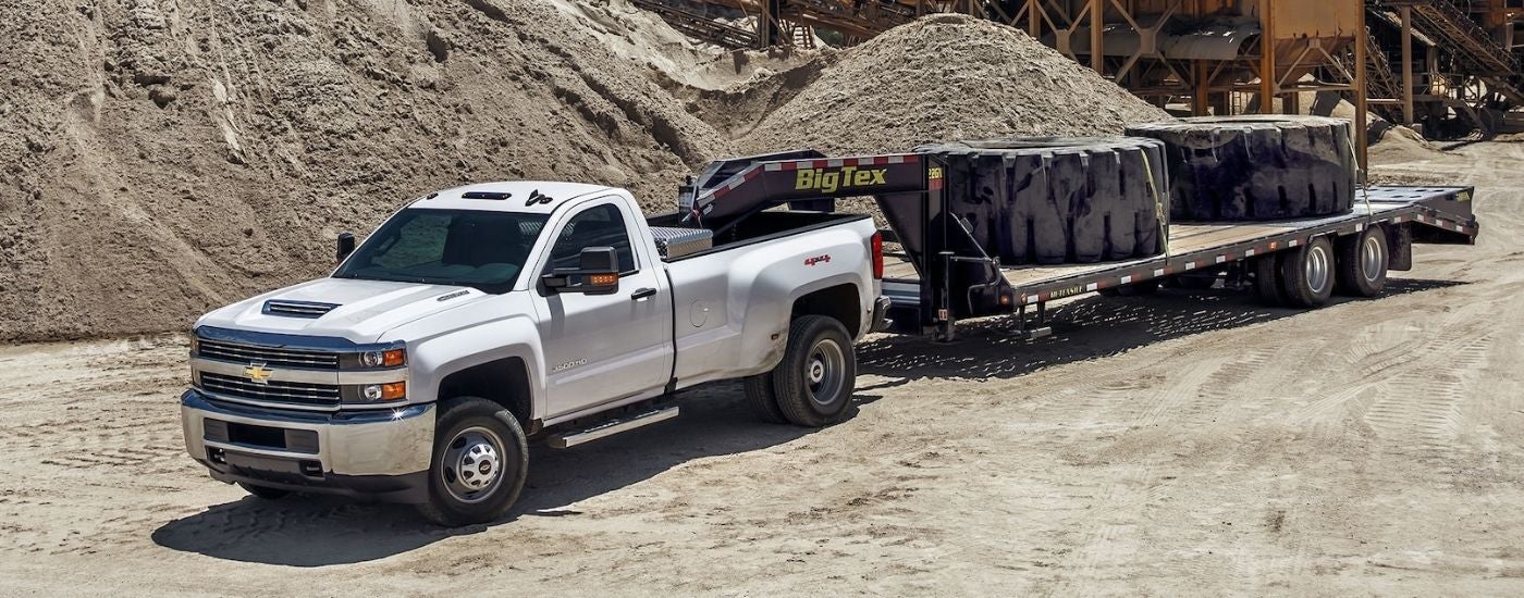 A silver 2018 Chevy Silverado 3500 HD is shown towing large tires.
