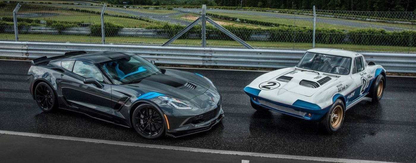 A grey 2017 Chevy Corvette Grand Sport and a white 1965 Corvette parked together on a race track.
