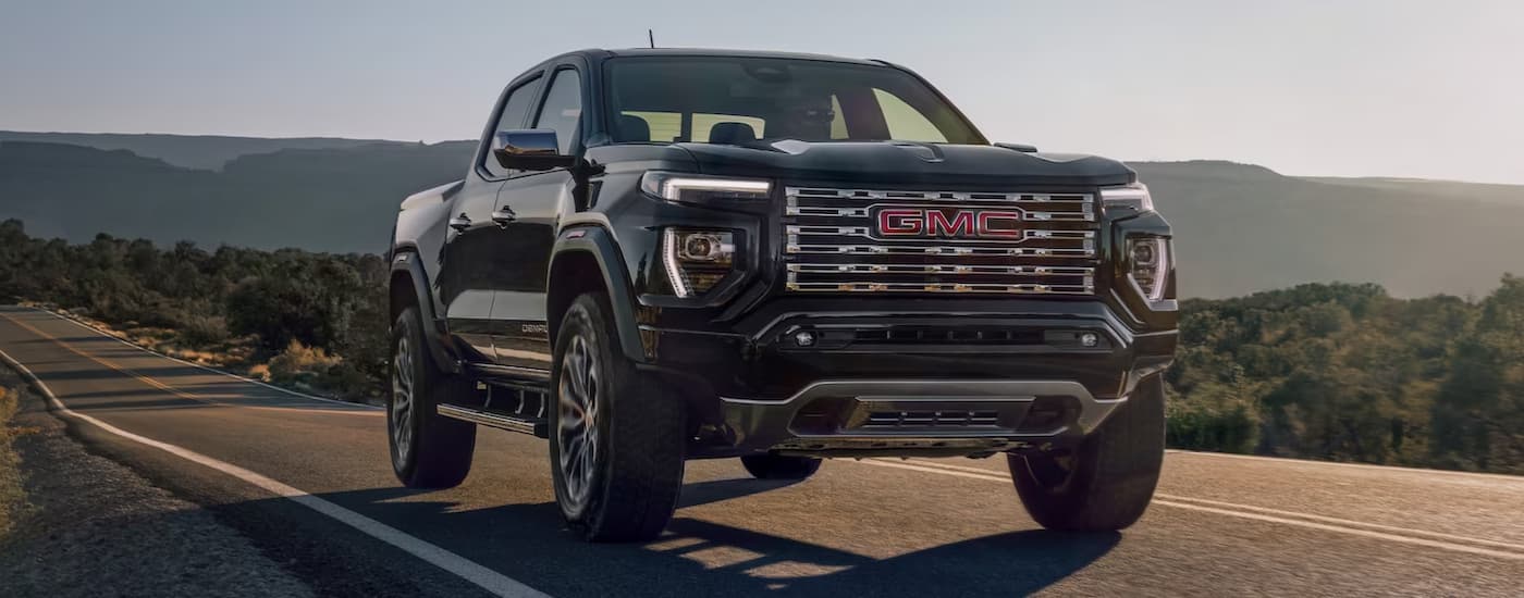 A black 2023 GMC Canyon Denali is shown driving on an open road after viewing trucks for sale.