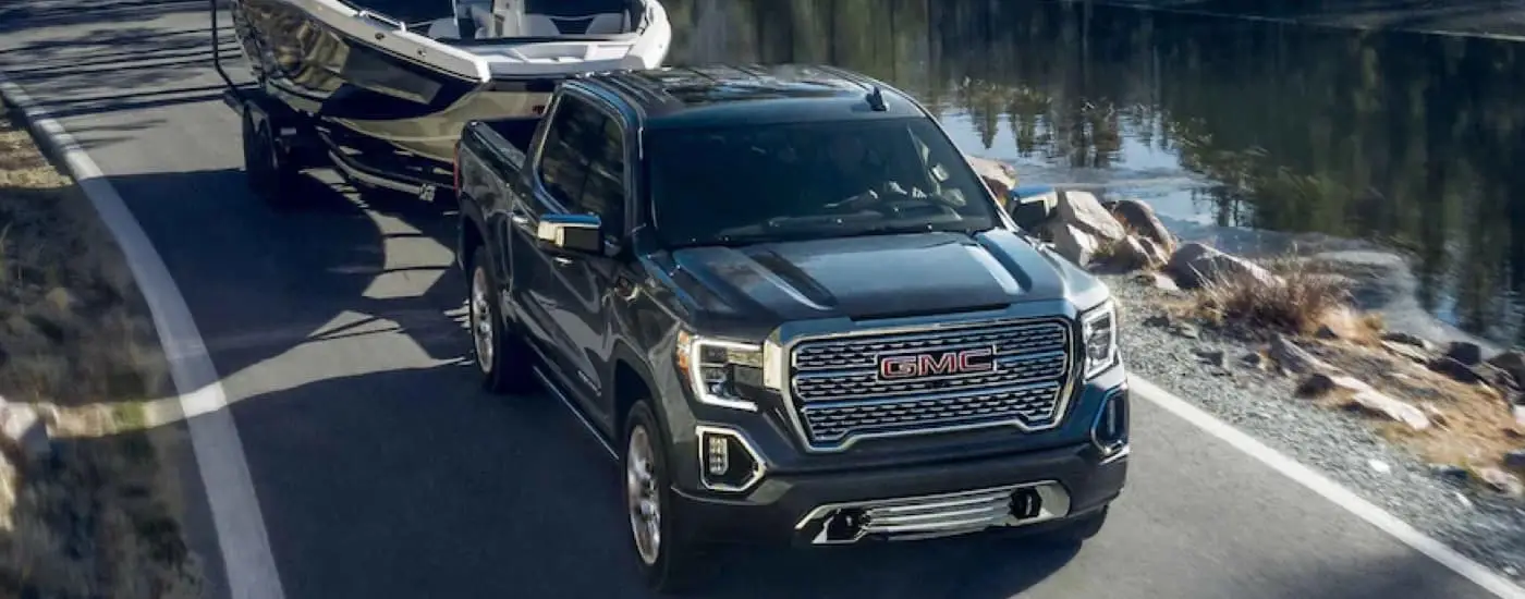 Black 2022 GMC Sierra 1500 Limited towing a boat next to river.