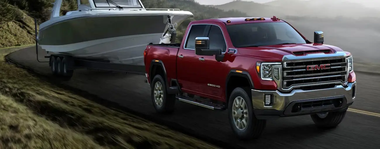 Red 2020 GMC Sierra 2500 towing a small boat on a winding road
