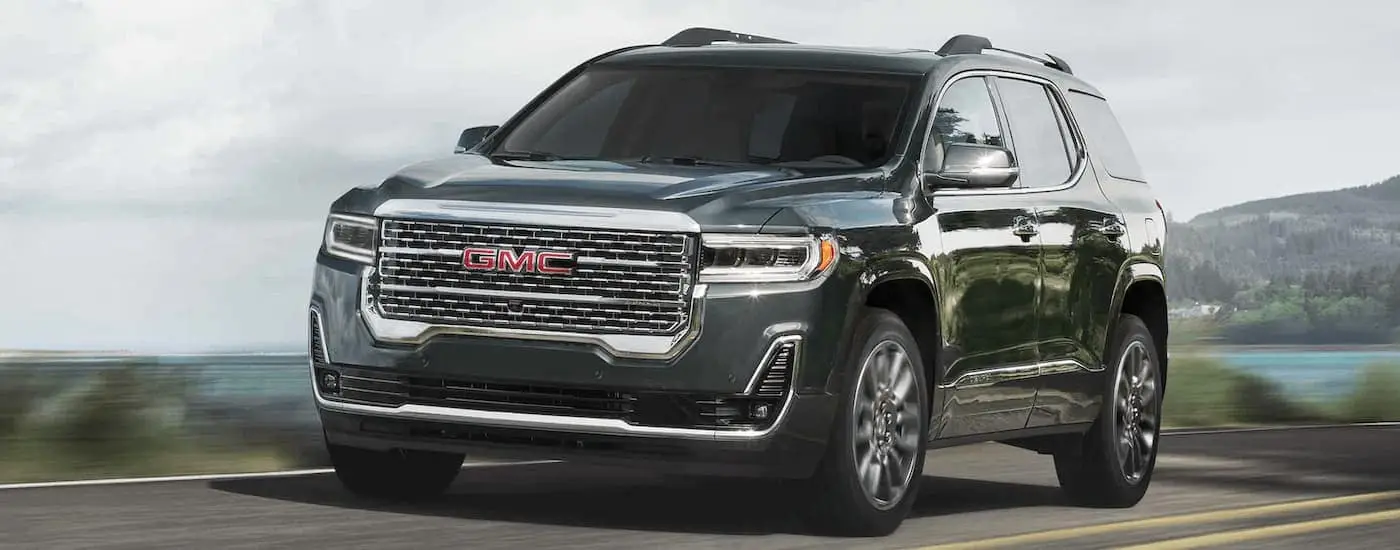 Grey 2023 GMC Acadia driving past a lake