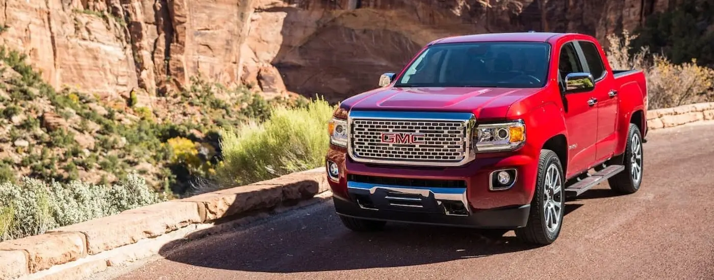 A red 2019 GMC Canyon Denali driving past rock walls after leaving a used truck dealer.