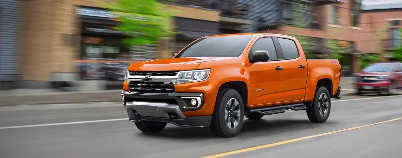 An orange 2021 Chevy Colorado Z71 driving on a street after leaving a dealer that has used Chevy trucks for sale.