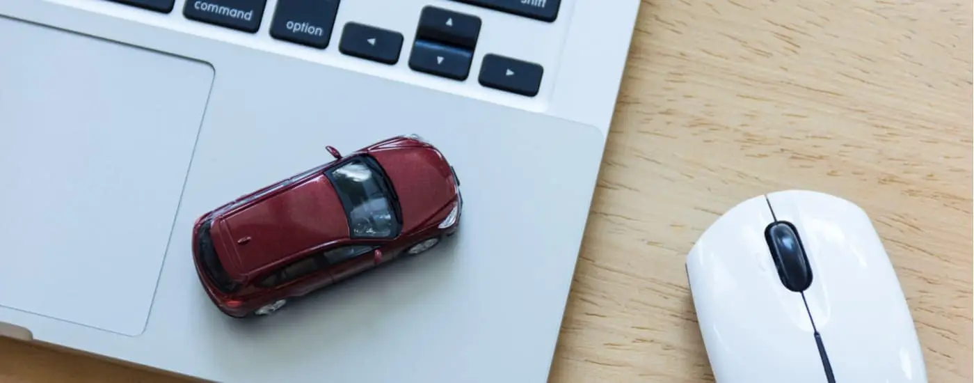A red toy car is shown on a laptop keyboard.